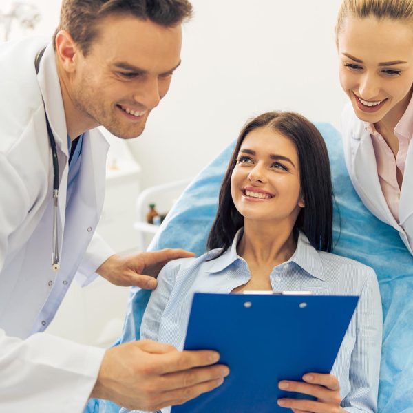 Beautiful female patient and two doctors are looking at folder with documents and smiling, at the doctors office